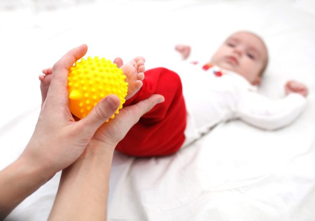 Baby feet in mommys hands. Massaging Feet with yellow ball. Concept of Love